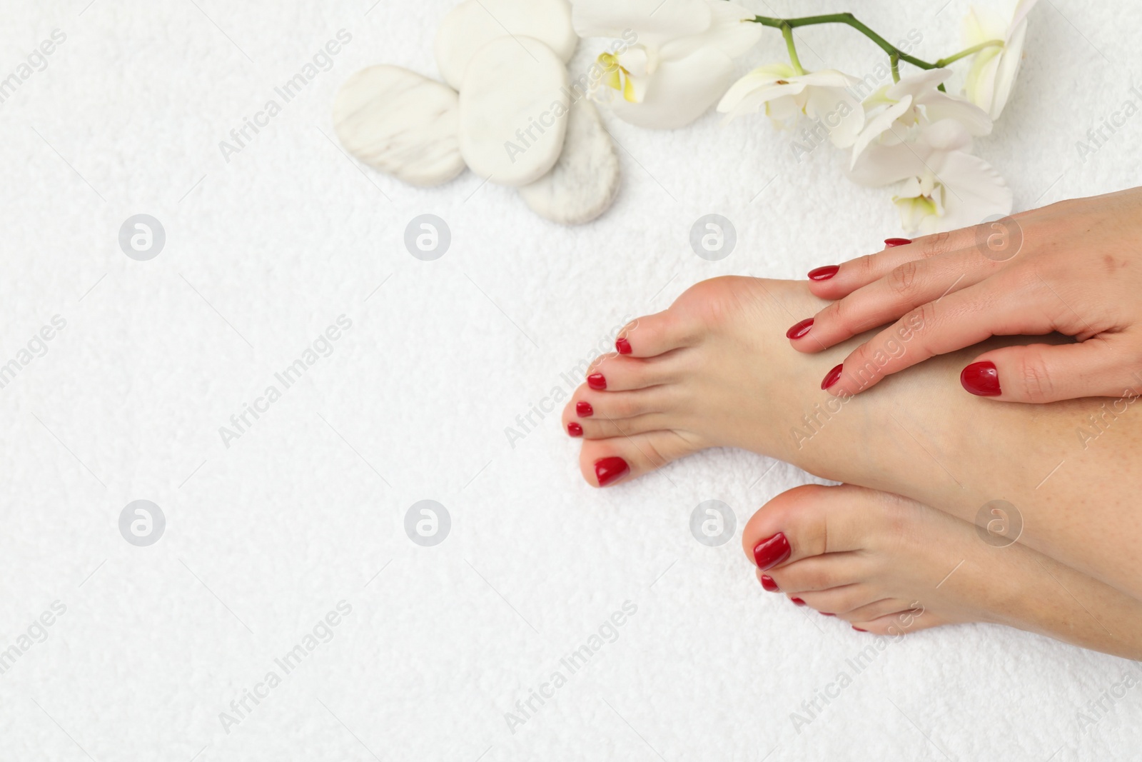 Photo of Woman with stylish red toenails after pedicure procedure and orchid flowers on white terry towel, top view. Space for text