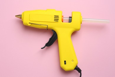 Photo of Yellow glue gun with stick on pink background, top view