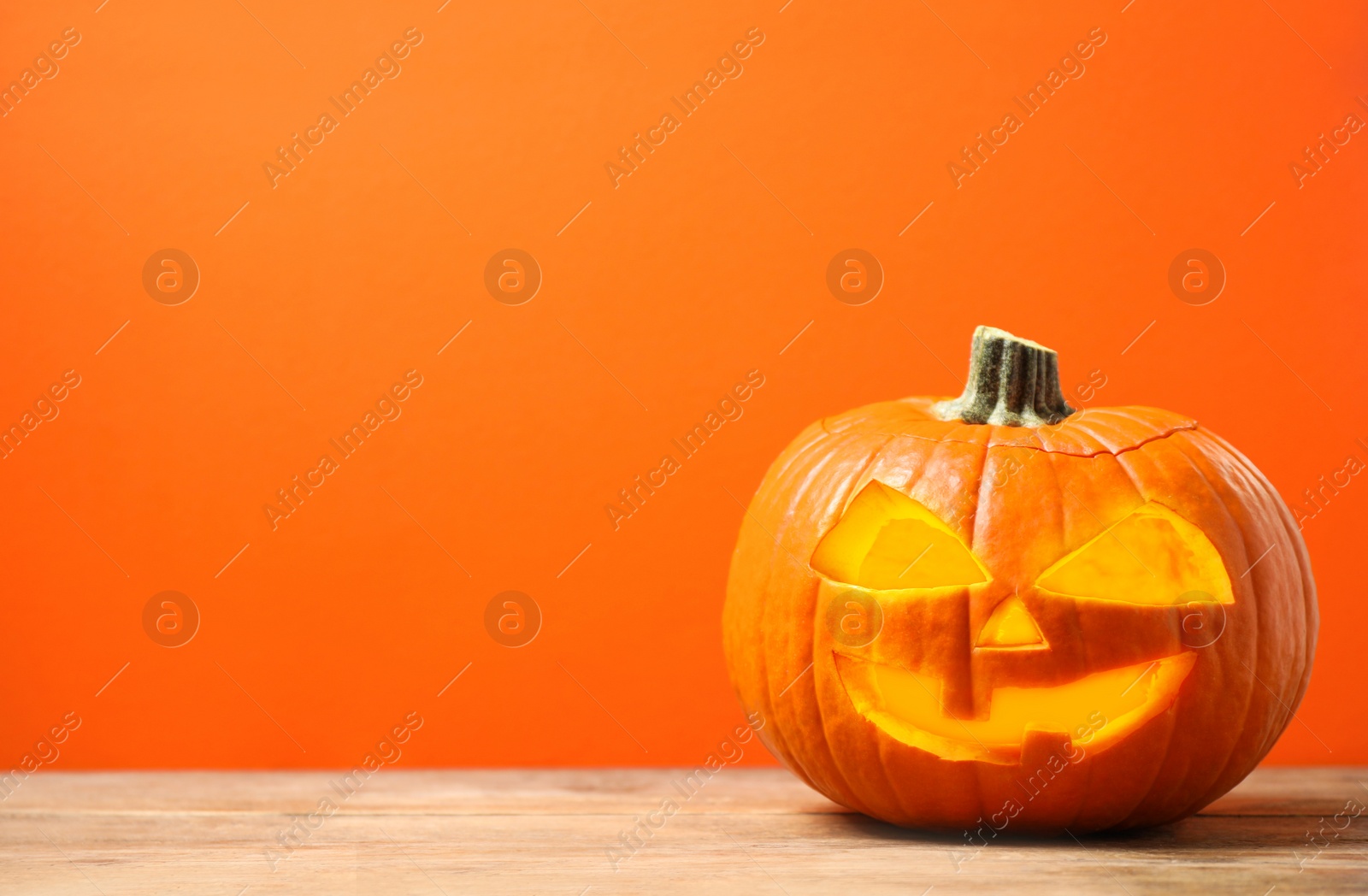 Photo of Scary jack o'lantern pumpkin on orange background, space for text. Halloween decor