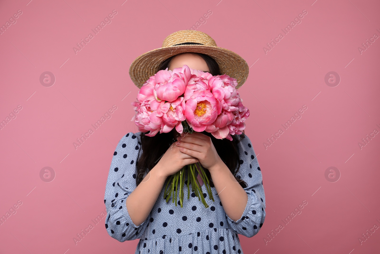 Photo of Young woman covering her face with bouquet of peonies on pink background