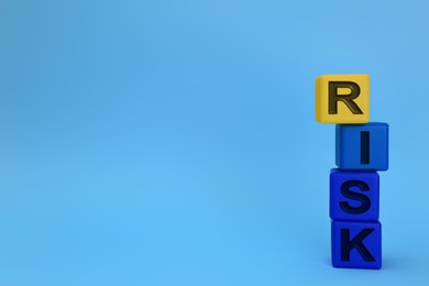 Photo of Stack of color wooden cubes with word Risk on light blue background. Space for text