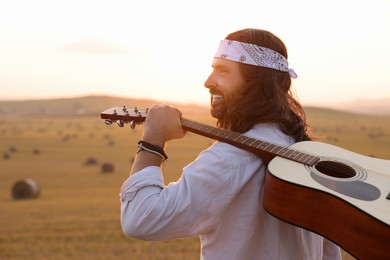 Photo of Portrait of happy hippie man with guitar in field, space for text