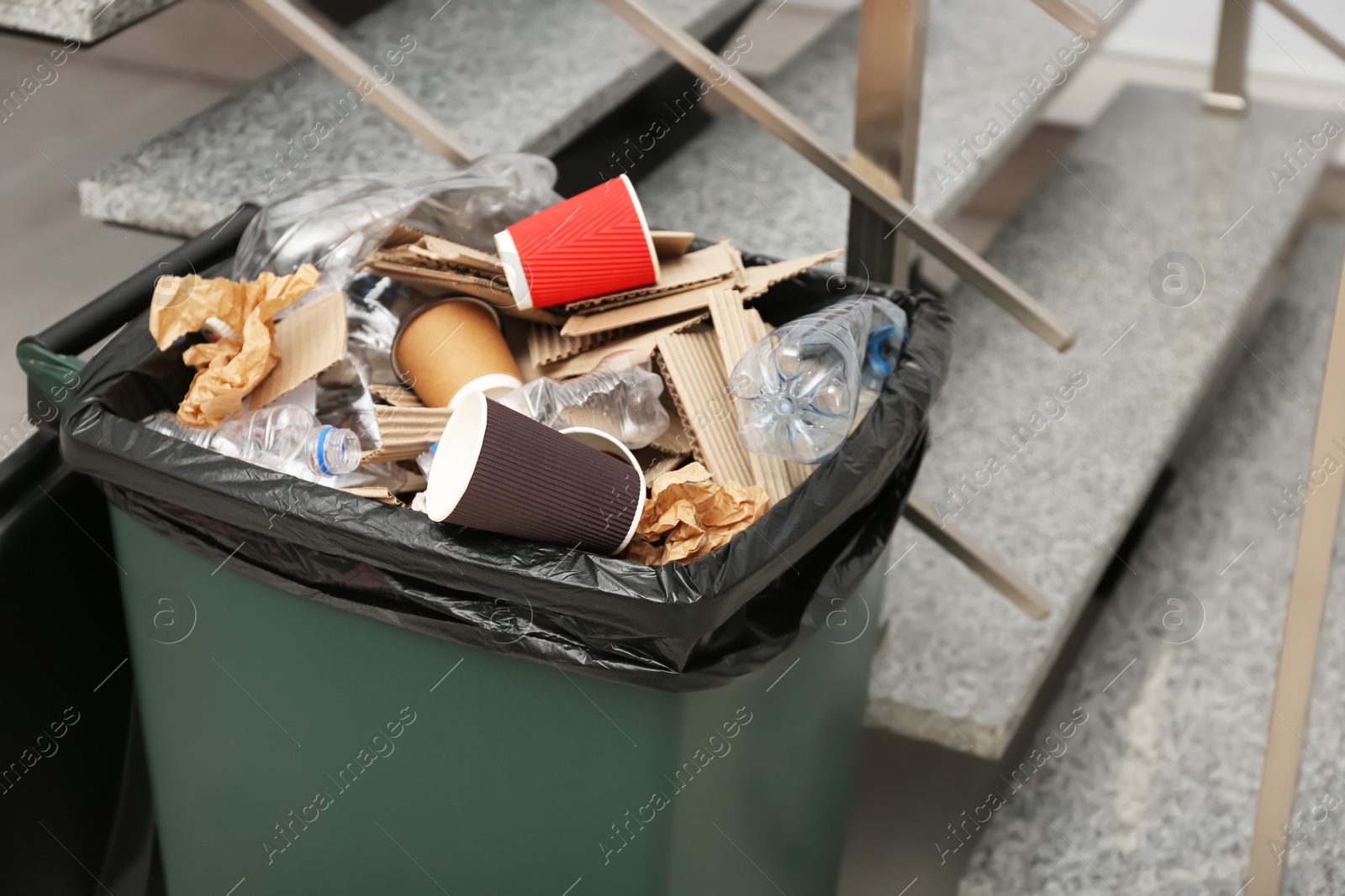 Photo of Full trash bin near stair way indoors. Waste recycling