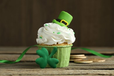 Photo of St. Patrick's day party. Tasty cupcake with green leprechaun hat topper on wooden table, closeup