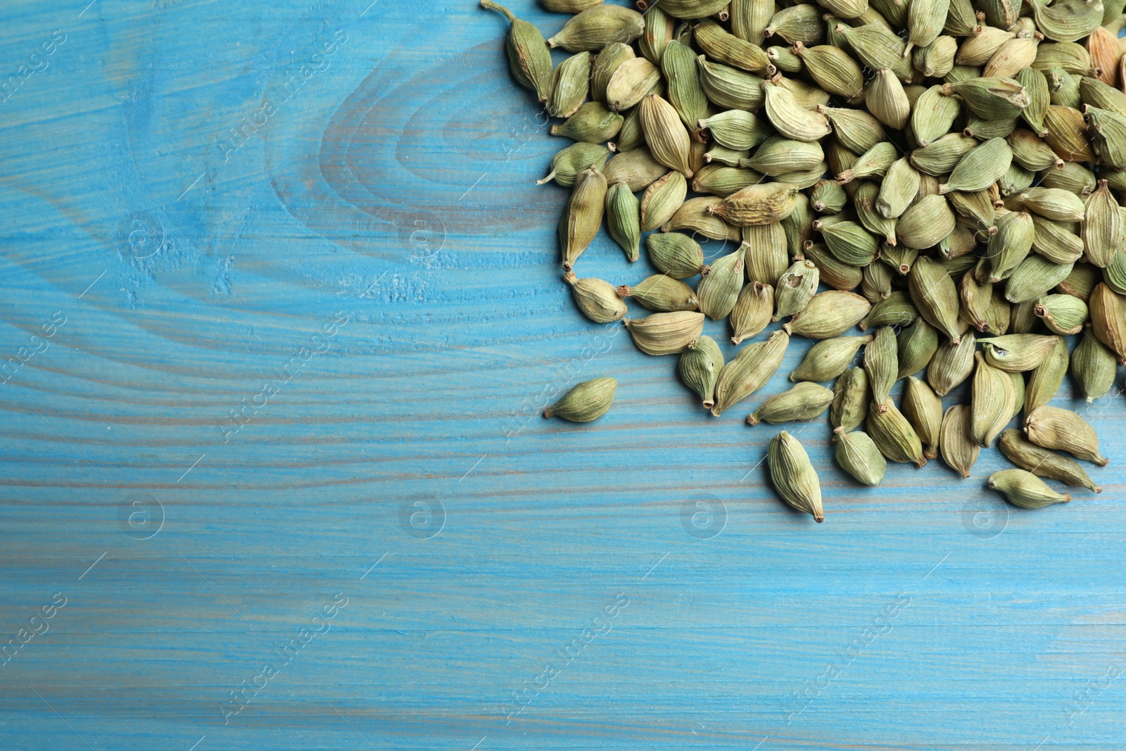 Photo of Pile of dry cardamom pods on light blue wooden table, top view. Space for text