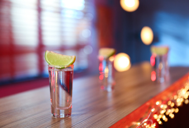 Photo of Mexican Tequila shot with salt and lime slice on bar counter. Space for text