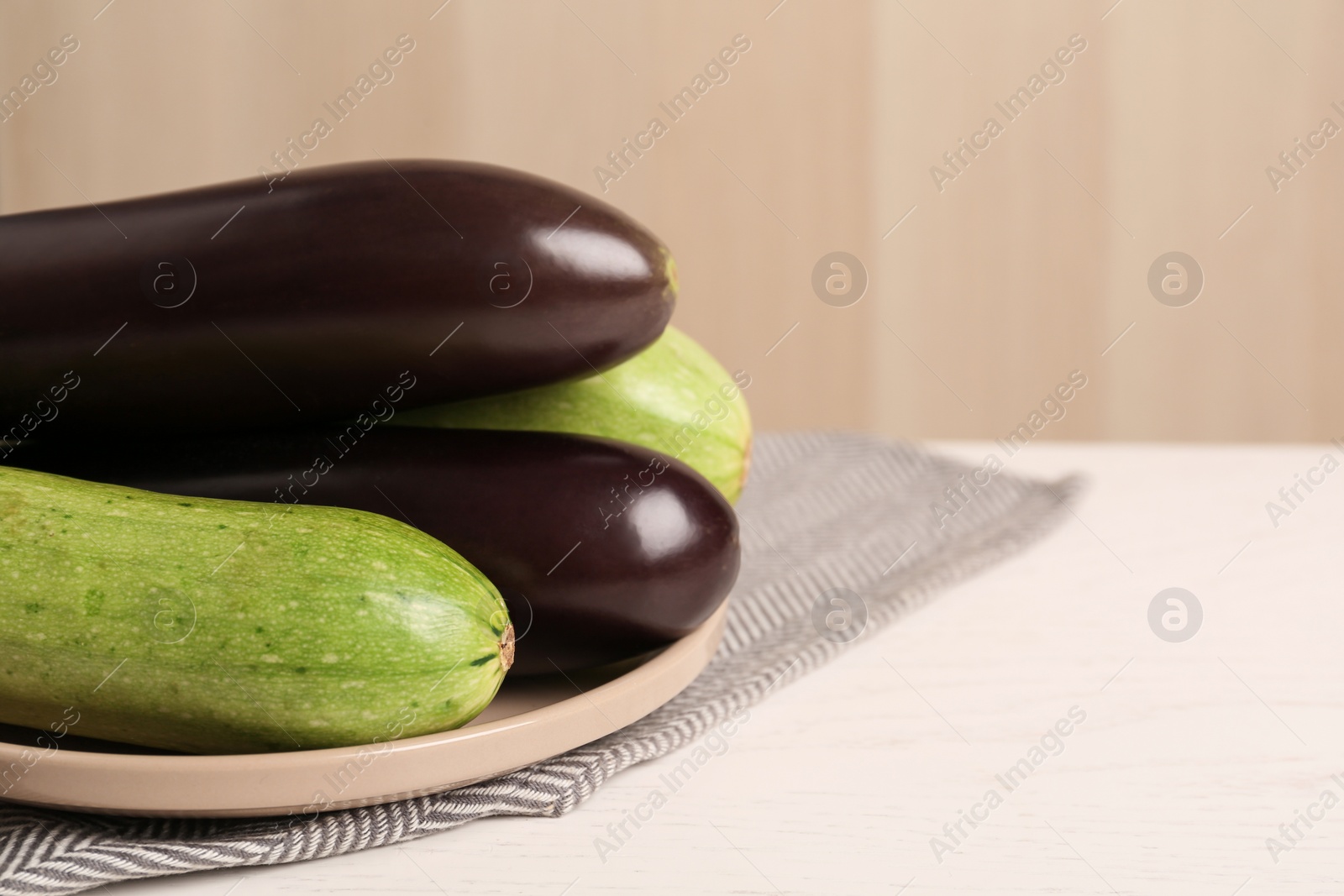 Photo of Fresh eggplants and zucchinis on white wooden table, closeup. Space for text