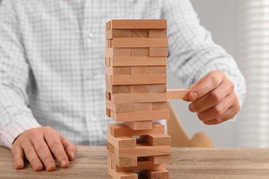 Photo of Playing Jenga. Man removing block from tower at wooden table indoors, closeup