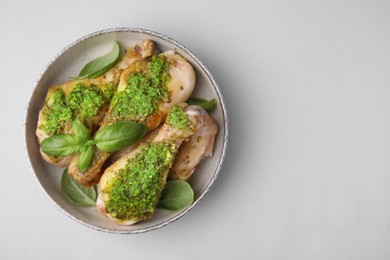 Photo of Delicious fried chicken drumsticks with pesto sauce and basil in bowl on light gray table, top view. Space for text