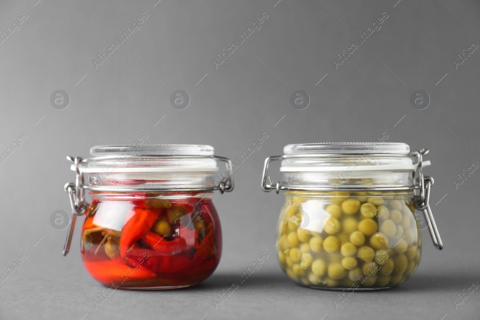 Photo of Jars of pickled red hot chili peppers and peas on grey background
