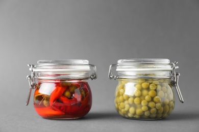 Photo of Jars of pickled red hot chili peppers and peas on grey background