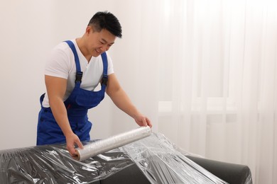 Worker wrapping sofa in stretch film indoors