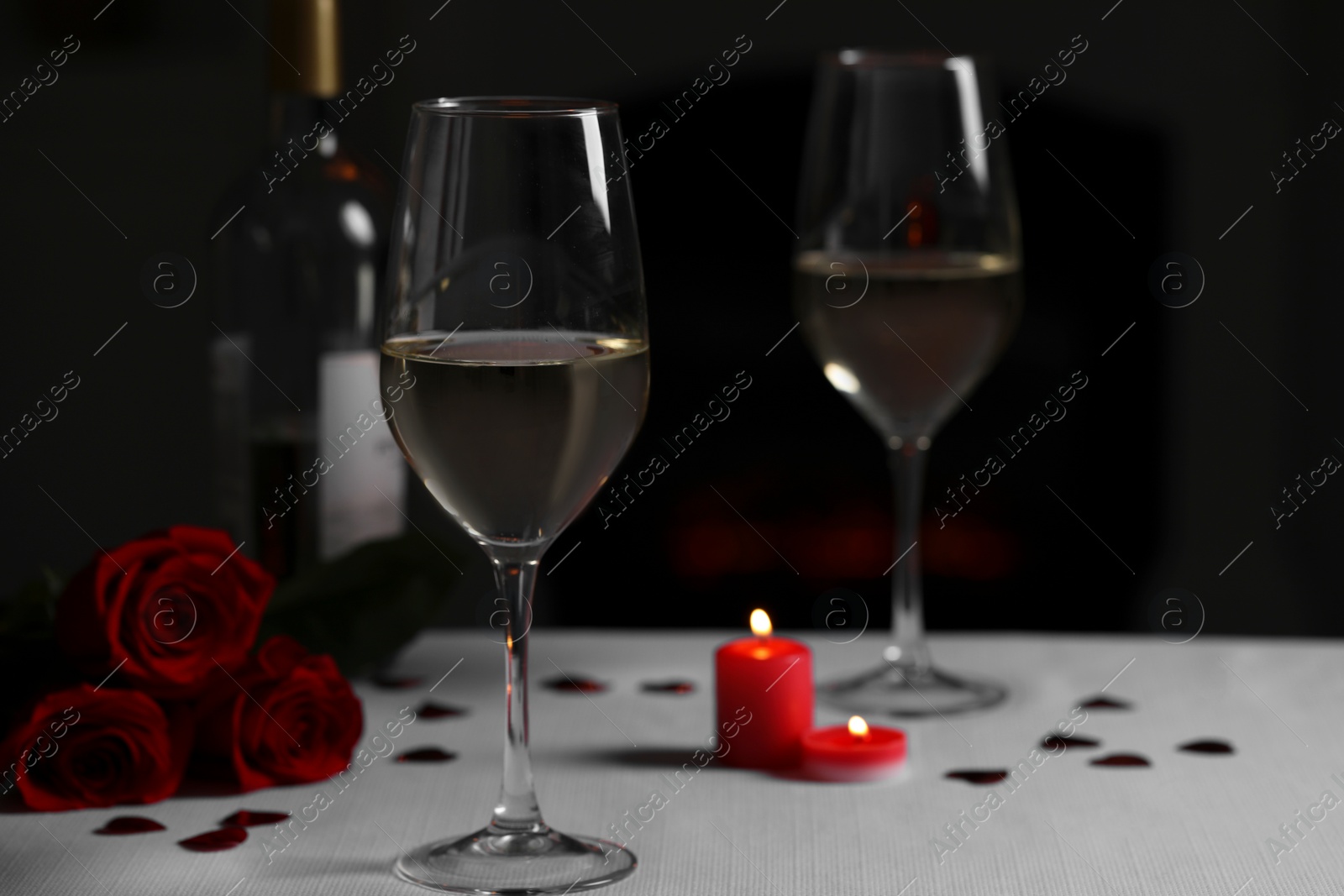 Photo of Glasses of white wine, rose flowers and burning candles on grey table against blurred background. Romantic atmosphere