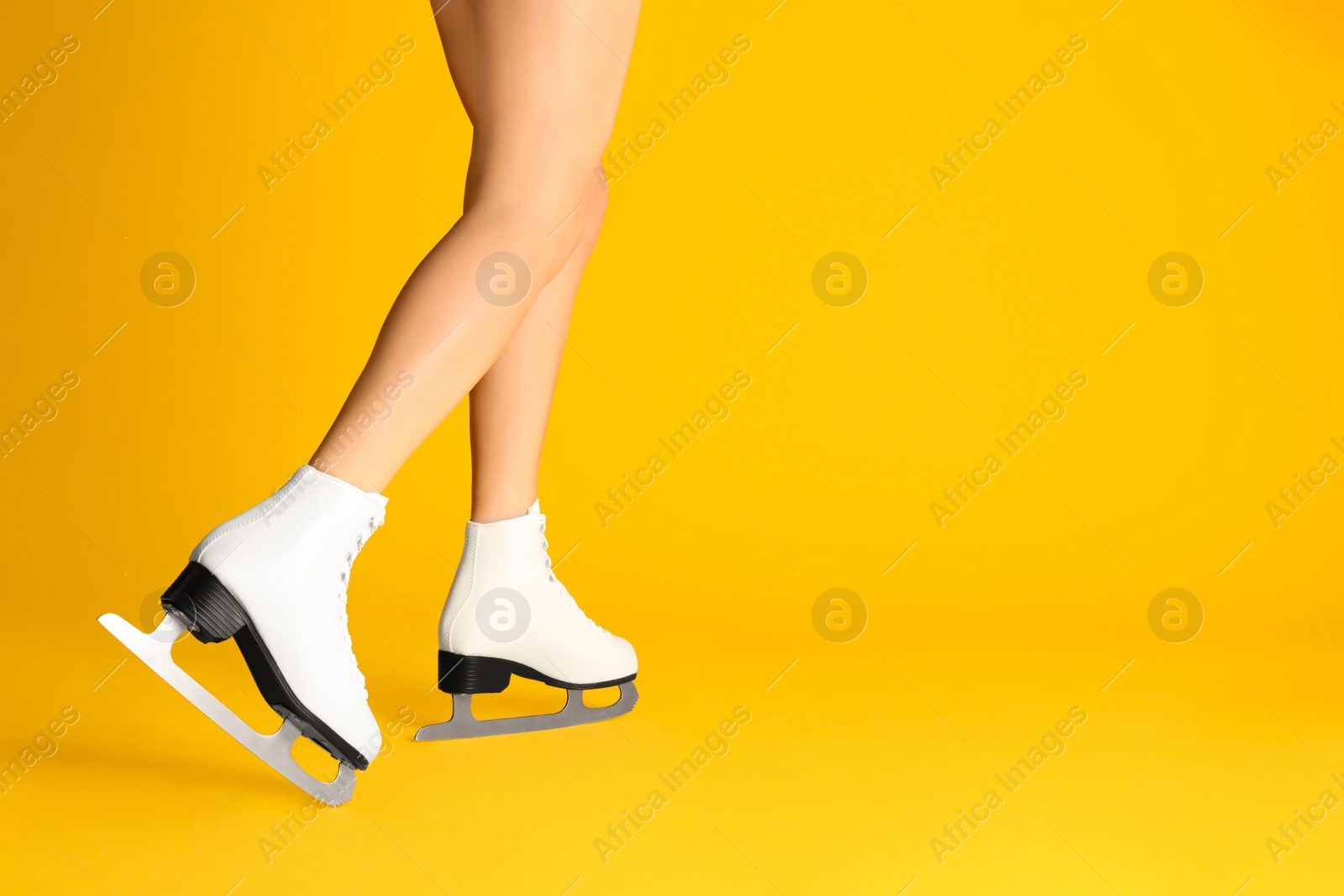 Photo of Woman in elegant white ice skates on yellow background, closeup of legs. Space for text