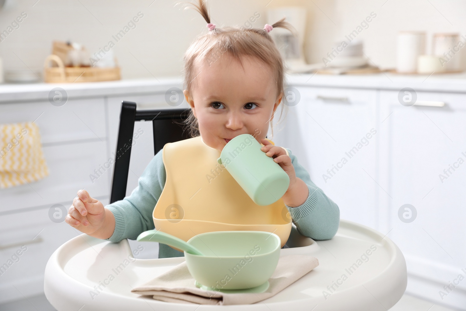 Photo of Cute little baby drinking from bottle in kitchen