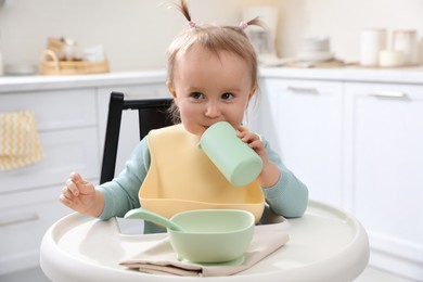 Cute little baby drinking from bottle in kitchen