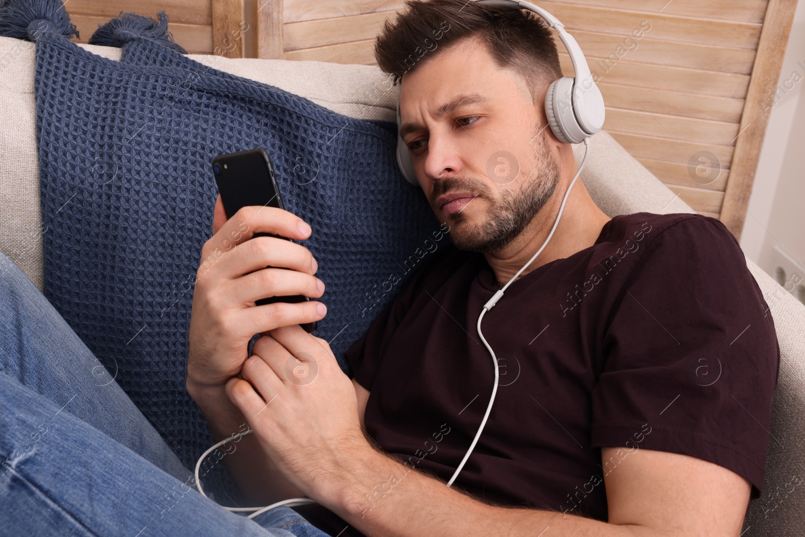 Photo of Upset man listening to music through headphones on sofa at home. Loneliness concept