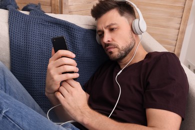 Photo of Upset man listening to music through headphones on sofa at home. Loneliness concept