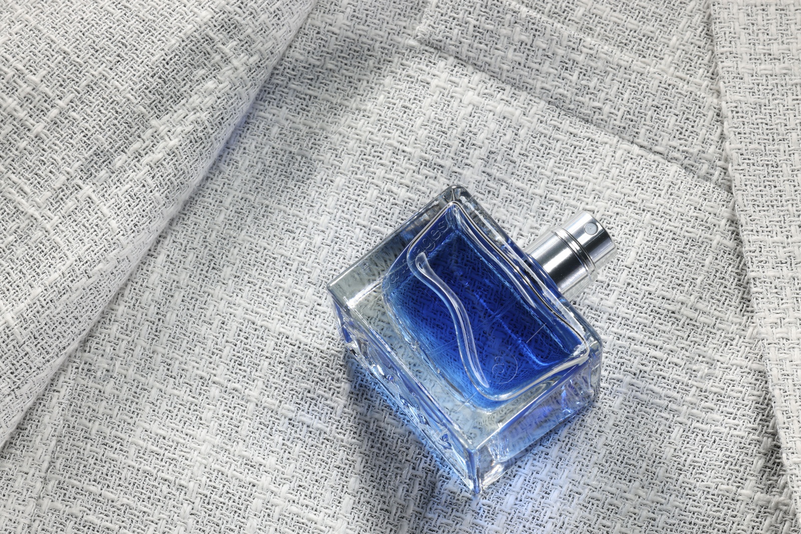 Photo of Luxury men's perfume in bottle on grey jacket, space for text