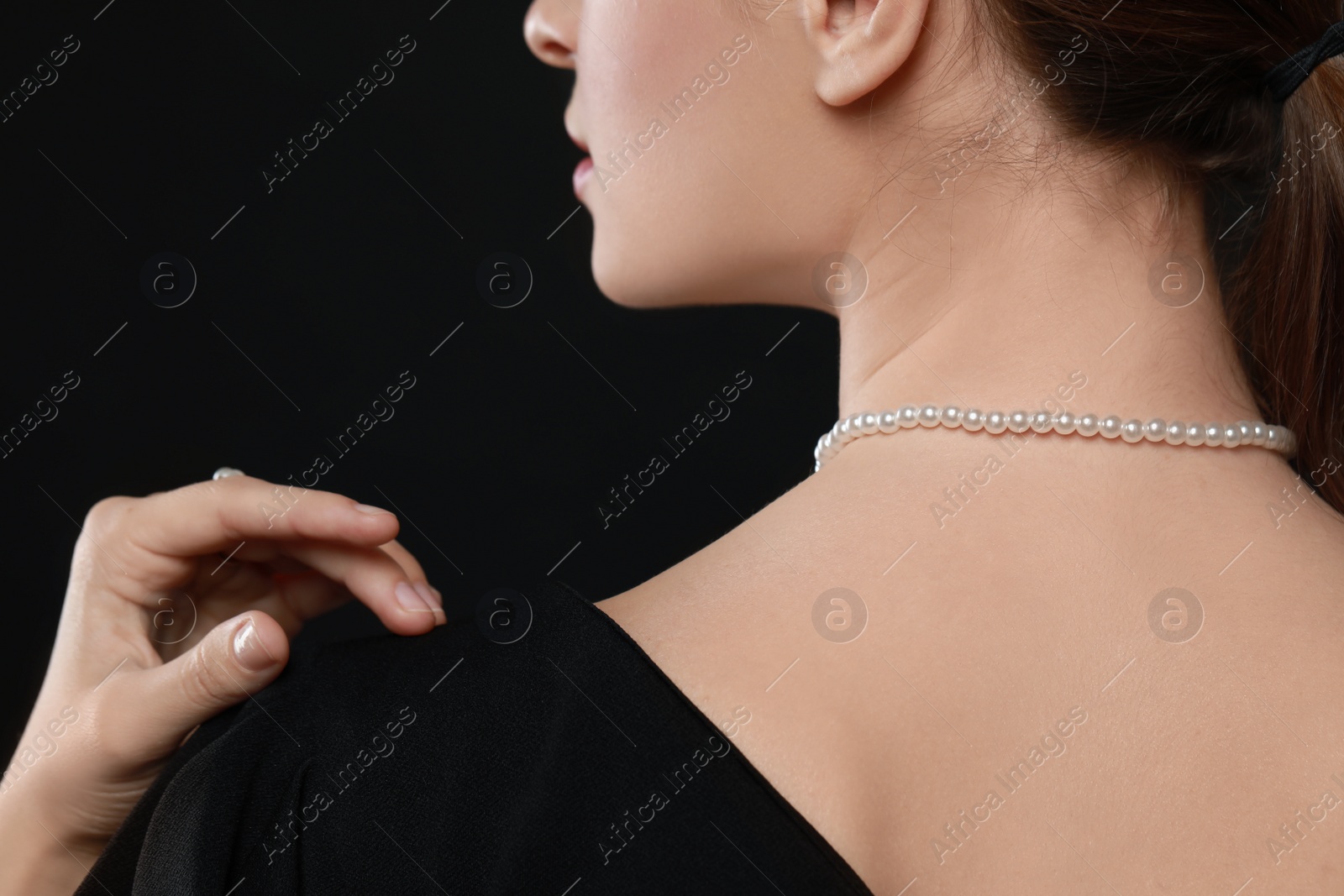 Photo of Young woman wearing elegant pearl necklace on black background, closeup