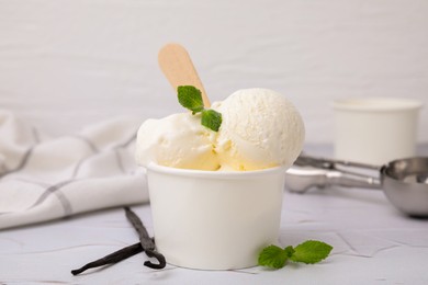 Photo of Delicious ice cream with mint and vanilla pods on white textured table, closeup