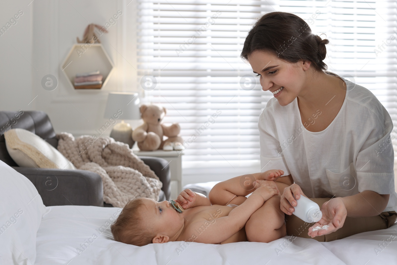 Photo of Mother with dusting powder near her cute baby at home, space for text