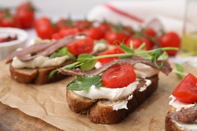 Photo of Delicious bruschettas with anchovies, tomatoes, microgreens and cream cheese on wooden board, closeup