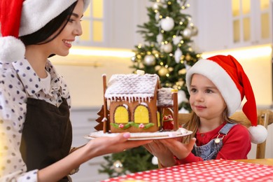 Mother and daughter with gingerbread house indoors