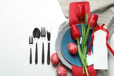 Festive Easter table setting with blank card and flowers on wooden background, top view. Space for text