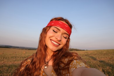 Beautiful happy hippie woman taking selfie in field