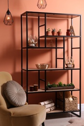Photo of Armchair near shelving with different decor, houseplants and firewood in room. Interior design