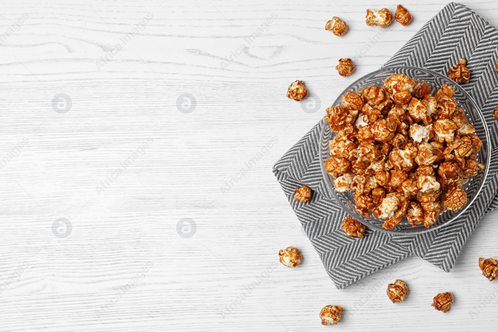 Photo of Bowl with caramel popcorn on white wooden background, top view. Space for text