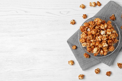 Bowl with caramel popcorn on white wooden background, top view. Space for text