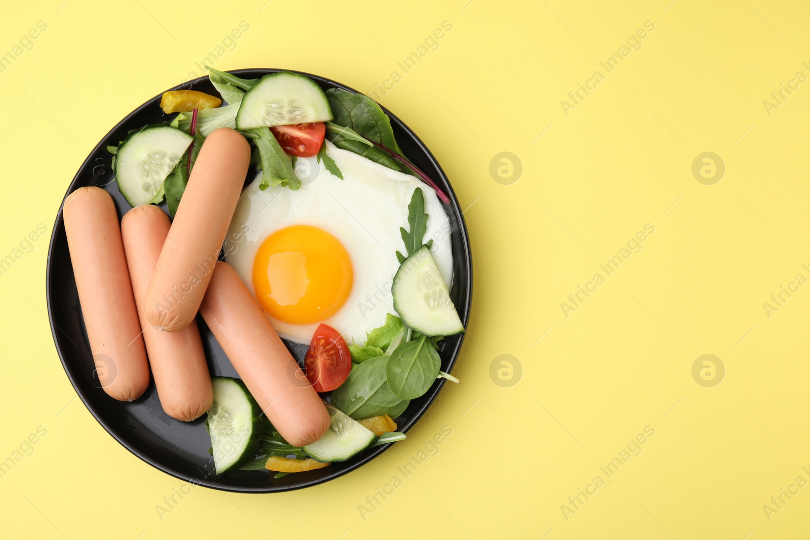 Photo of Delicious breakfast with boiled sausages and fried egg on yellow background, top view. Space for text