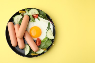 Photo of Delicious breakfast with boiled sausages and fried egg on yellow background, top view. Space for text