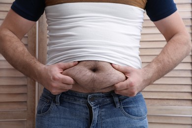 Photo of Man wearing tight t-shirt near wooden folding screen, closeup. Overweight problem