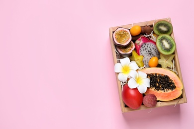 Different tropical fruits in wooden box on pink background, top view. Space for text