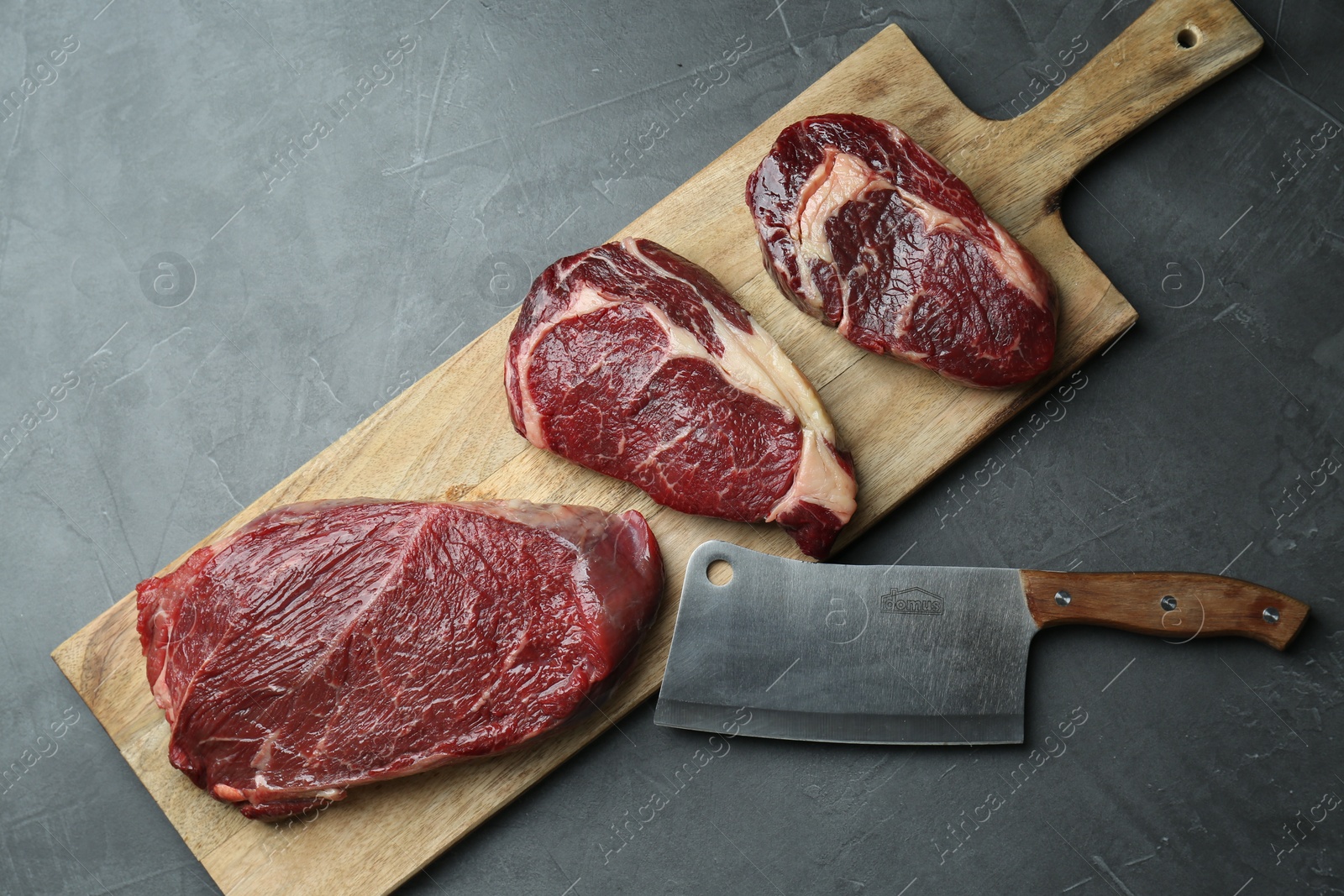 Photo of Wooden board with pieces of raw beef meat and knife on grey table, flat lay