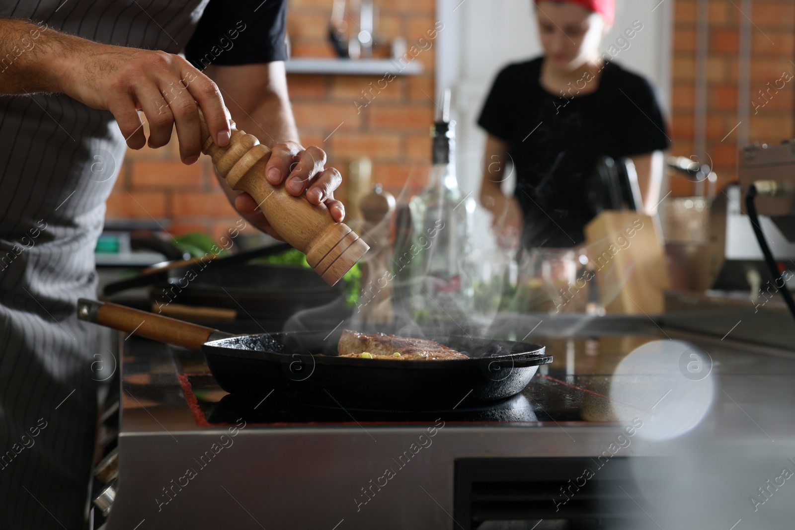 Photo of Professional chef cooking meat on stove in restaurant kitchen, closeup