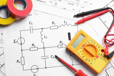 Digital multimeter and tapes on paper sheets, flat lay. Electrician's supplies