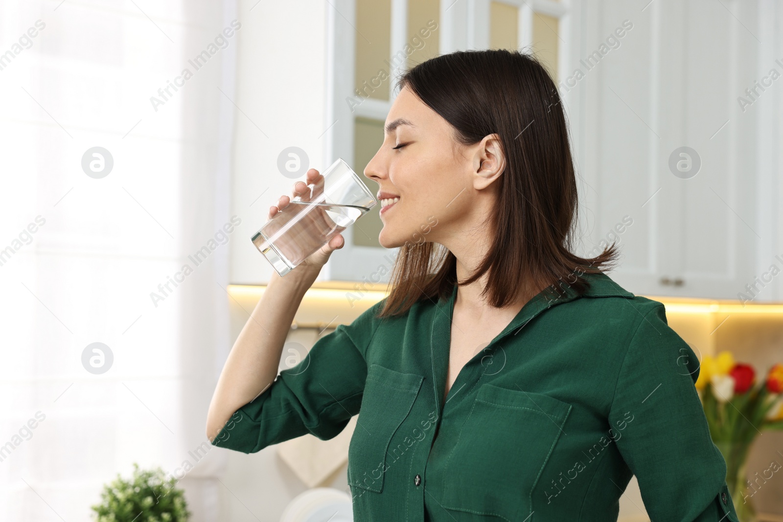 Photo of Young woman drinking clean water in kitchen