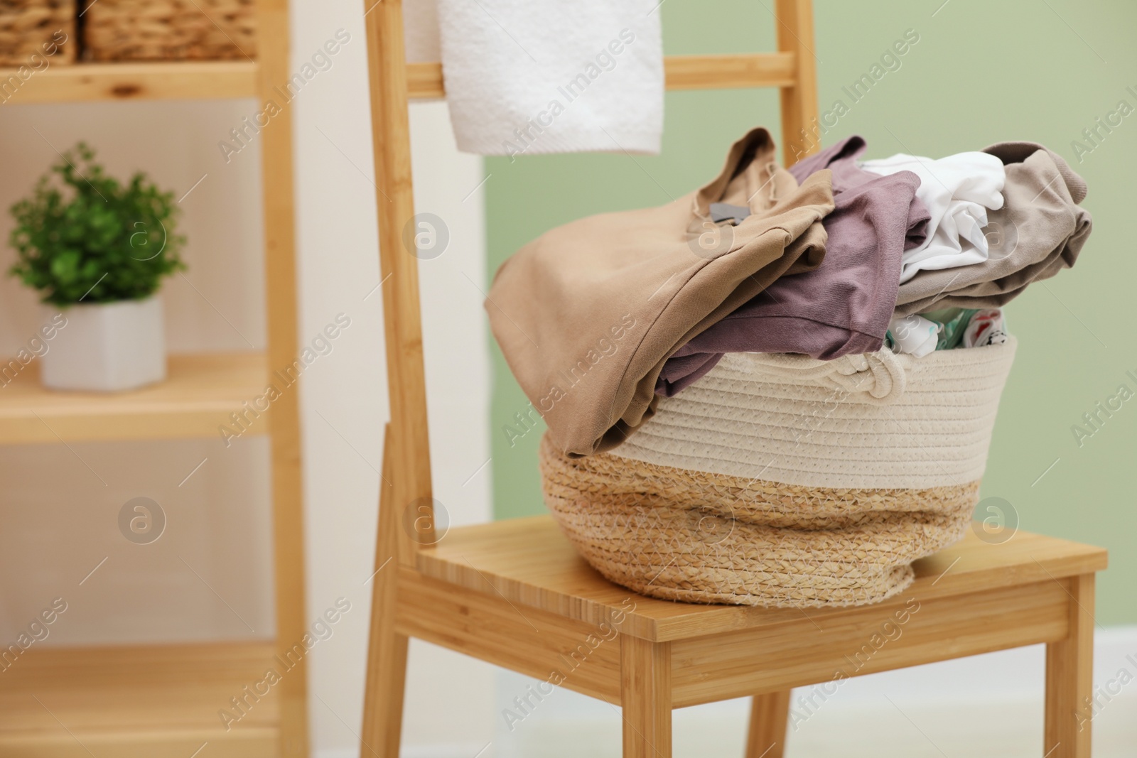 Photo of Laundry basket filled with clothes on chair in bathroom, closeup. Space for text