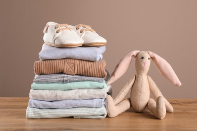 Photo of Stack of baby boy's clothes, shoes and toy on wooden table against brown background, space for text