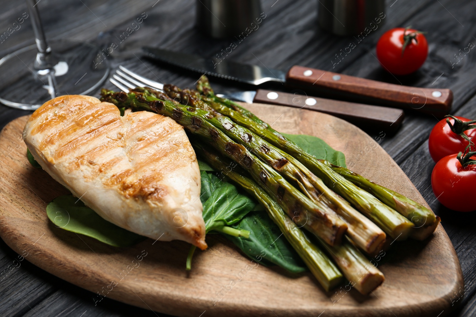 Photo of Tasty grilled chicken fillet served with asparagus on wooden board, closeup