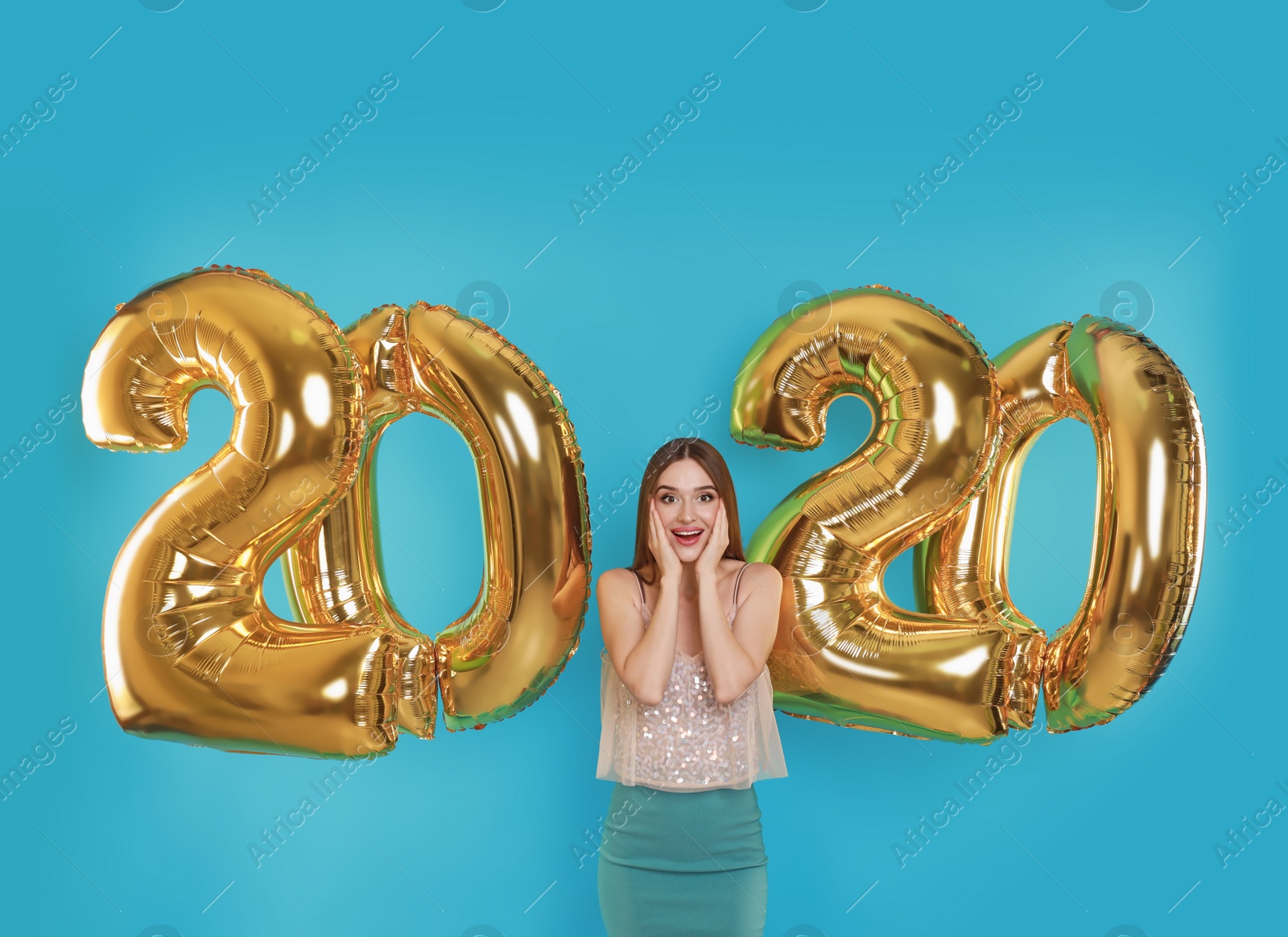 Photo of Excited young woman near golden 2020 balloons on turquoise background. New Year celebration