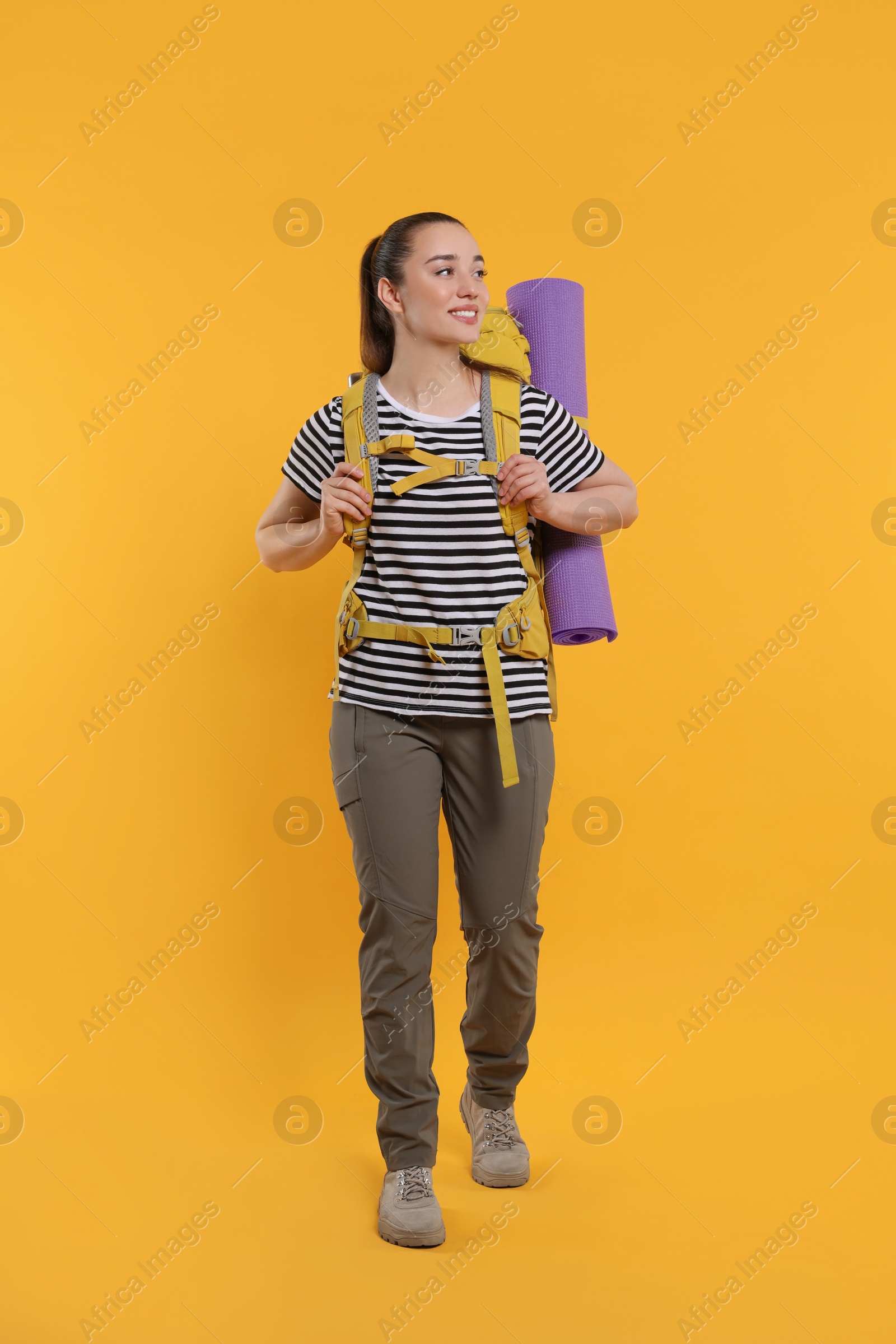 Photo of Smiling young woman with backpack walking on orange background. Active tourism