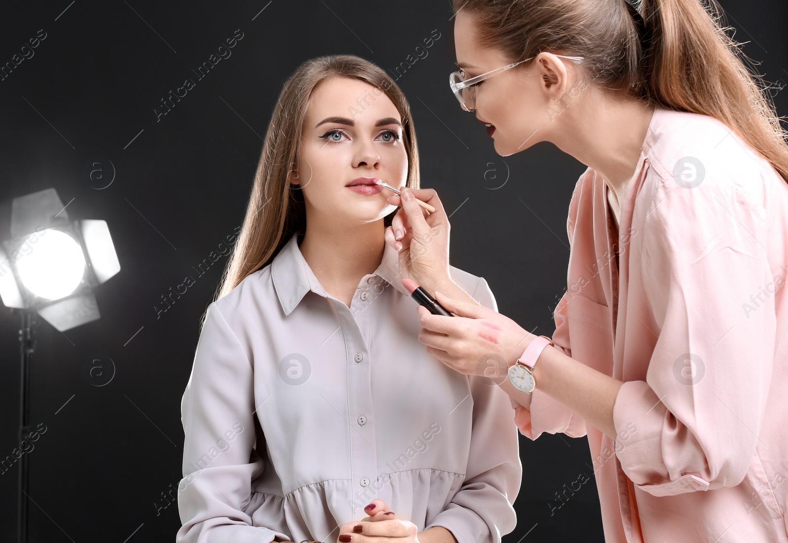 Photo of Professional makeup artist working with beautiful young woman in photo studio