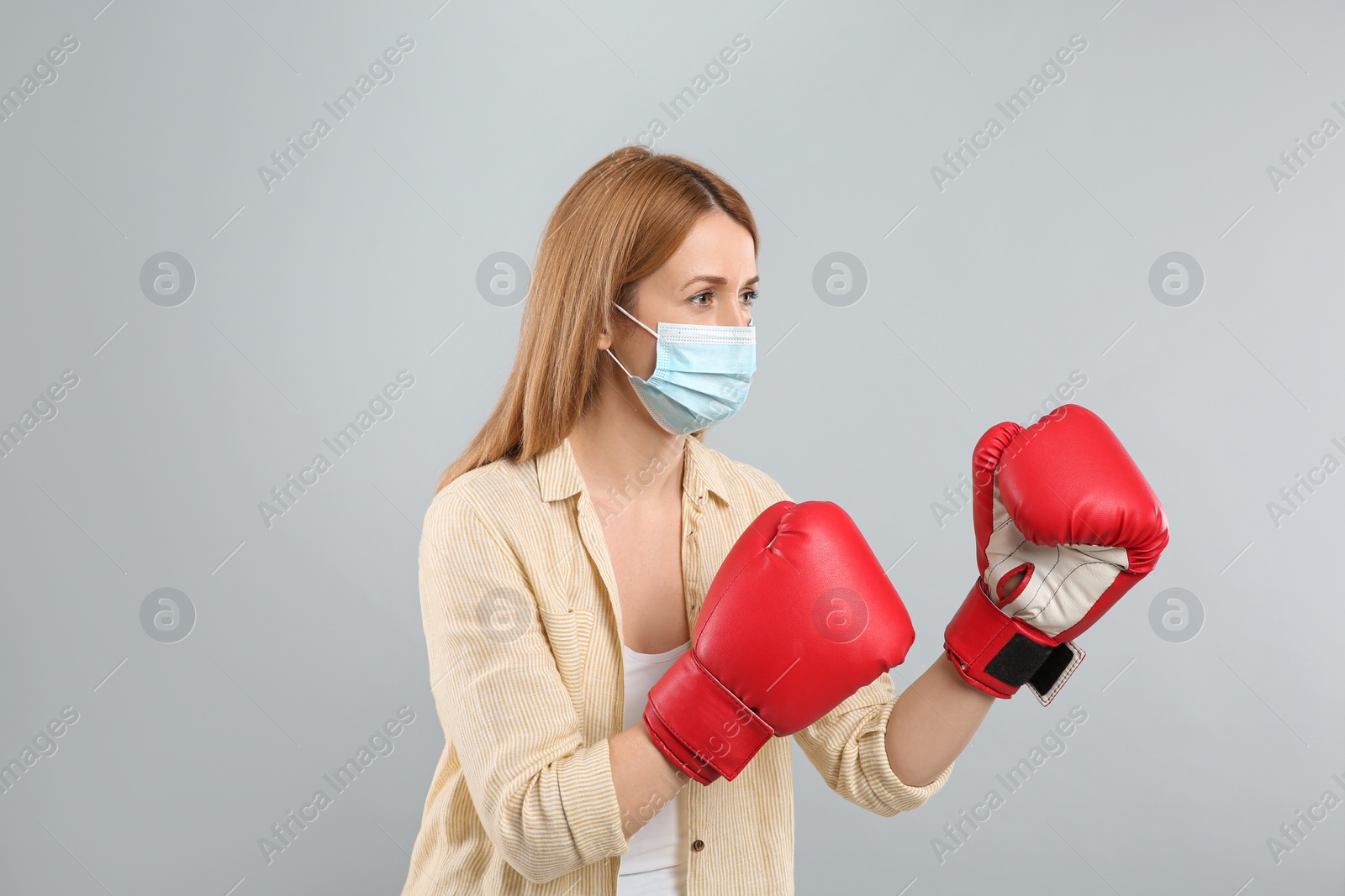 Photo of Woman with protective mask and boxing gloves on light grey background. Strong immunity concept