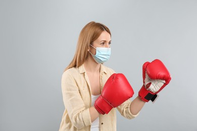 Woman with protective mask and boxing gloves on light grey background. Strong immunity concept