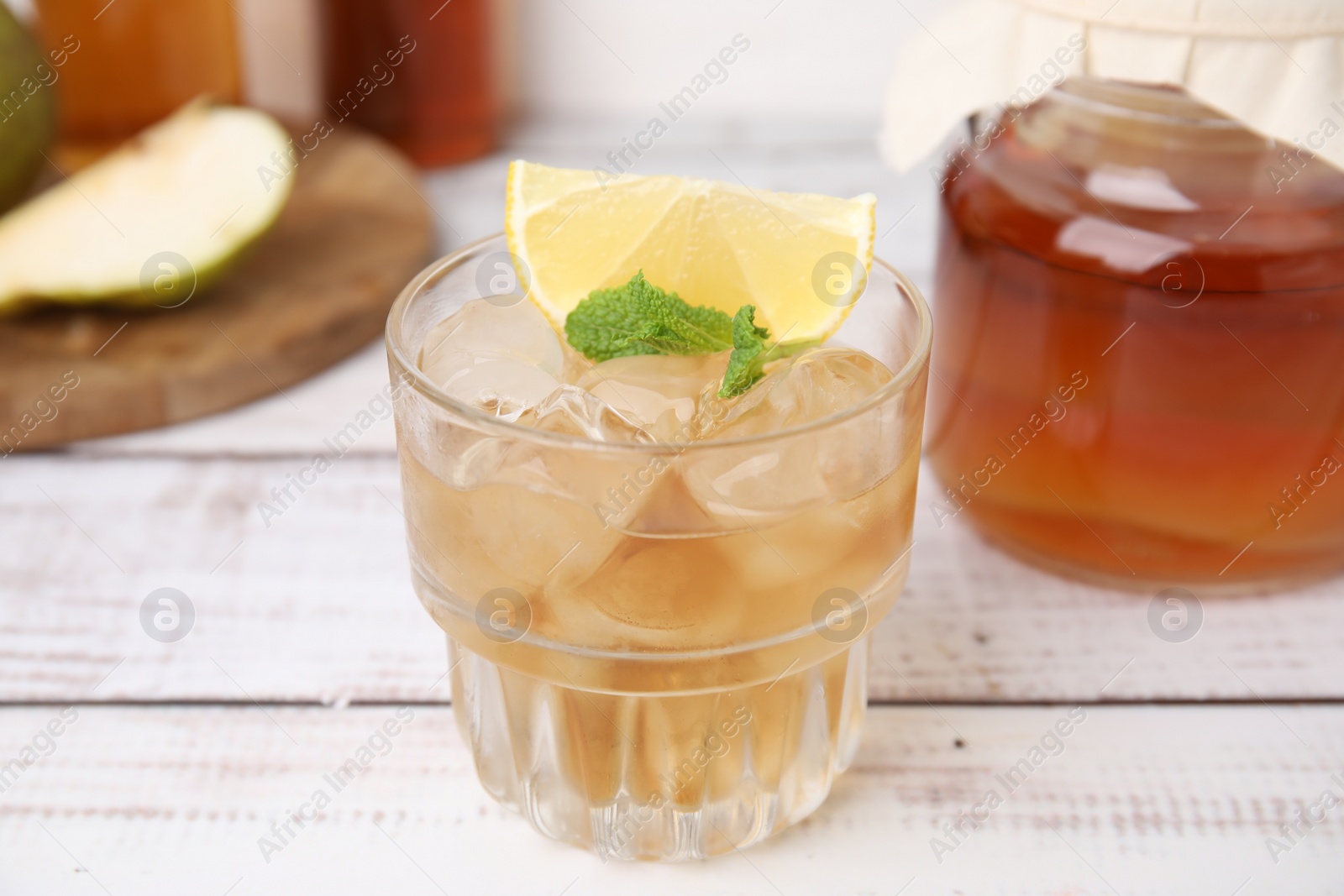 Photo of Tasty kombucha and ice cubes in glass on white wooden table, closeup